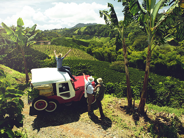 three people by a jeep admiring a Colombian coffee farm.