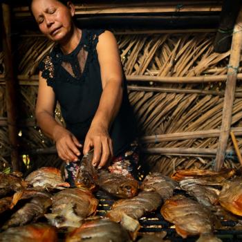 коренная женщина в хижине готовит еду из рыбы.
