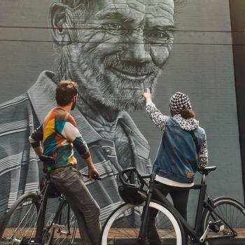 Paar auf einem Fahrrad mit dem Rücken zueinander, das ein kolumbianisches Street-Art-Wandgemälde betrachtet.