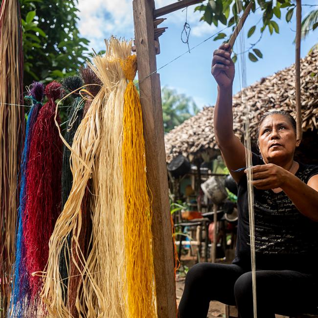 mujer campesina en rancheria tejiendo y haciendo artesanias de colombia.