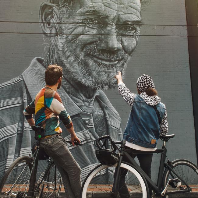 一对骑自行车的夫妇背对着对方看着哥伦比亚街头艺术壁画。